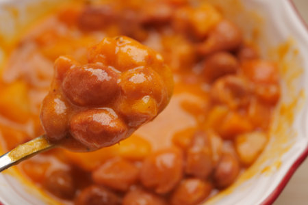 Warm bowl of baked beans served with spoon on a cozy tableの写真素材