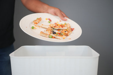 Person discarding leftover food in a waste binの写真素材