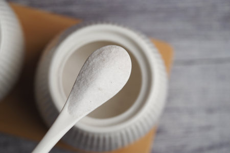 White sugar on a spoon next to a container on a tableの写真素材