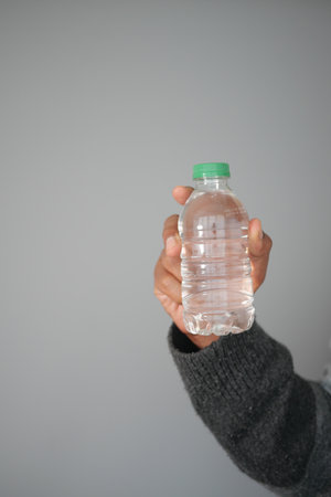 Holding a clear water bottle in a neutral settingの写真素材