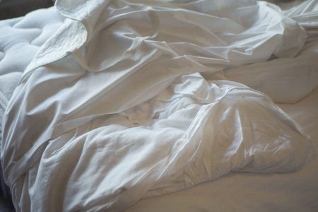 Soft white bedding on a cozy unmade bed in morning light