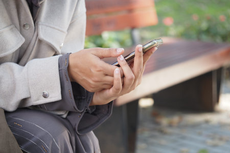Person using smartphone on a park bench in a sunny day