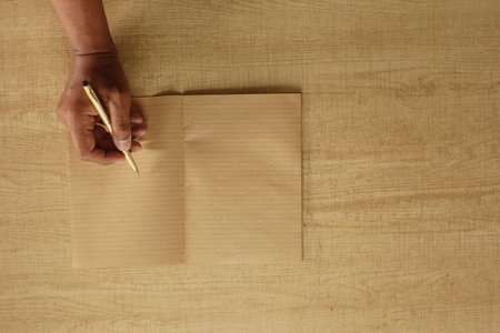 Person writing in a notebook on wooden table surface