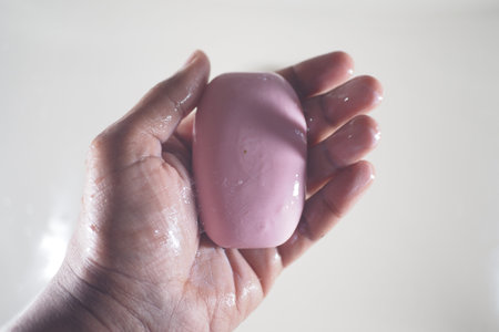 Hand holding pink soap in a bright bathroom setting