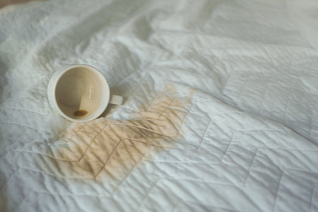 Coffee spills on white bedspread in morning lightの写真素材