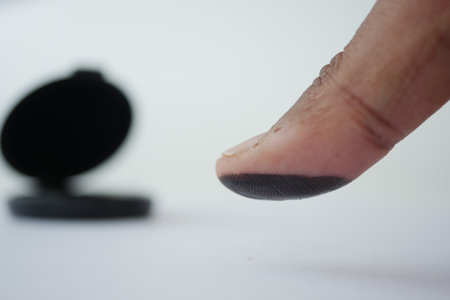 Finger with black ink near an open inkpad on a white surfaceの写真素材