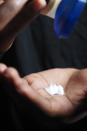 Hand dispensing cream in dim lighting during evening routineの写真素材