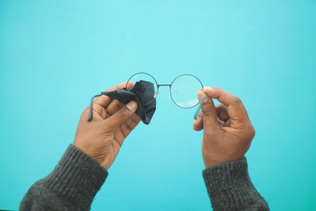 Hands cleaning round glasses against a blue backdropの写真素材