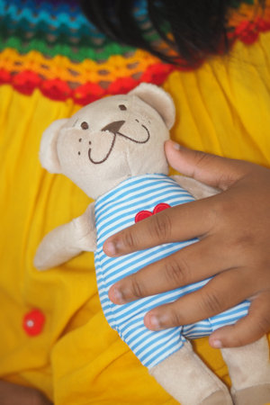 Child holds a teddy bear while wearing a colorful dressの写真素材