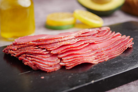 Sliced meat on a dark board with fresh ingredientsの写真素材