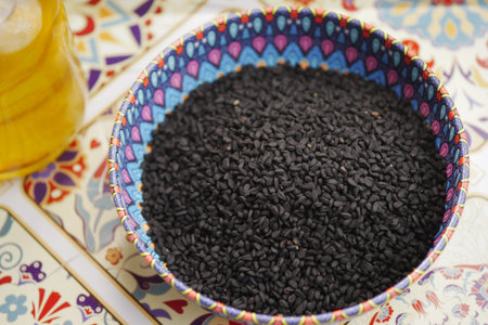 black cumin seed in a colorful bowl on a patterned tableの写真素材