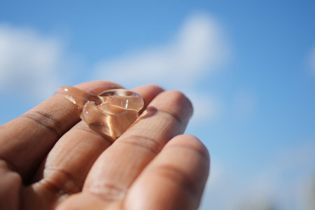 Hand holding aloe vera gel against blue skyの写真素材