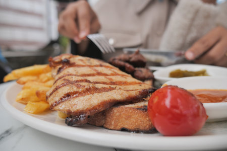 Grilled chicken served with fries and tomato at a restaurantの写真素材