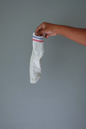 A hand holds a dirty white sock against a gray background