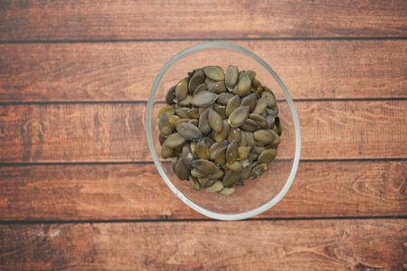 Healthy pumpkin seeds in a glass bowl on wooden tableの写真素材
