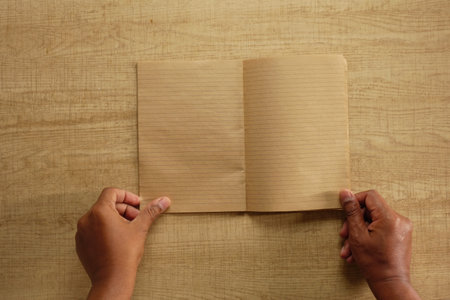 Hands holding a blank notebook on a wooden table