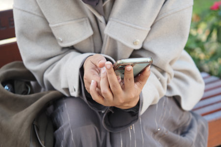 Person checking smartphone while sitting in a parkの写真素材