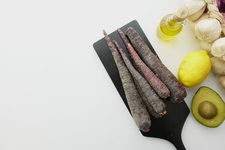 Fresh purple carrots, avocado, and garlic arranged on a cutting boardの写真素材