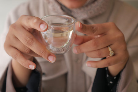 Holding a small glass of clear liquid in a cozy settingの写真素材