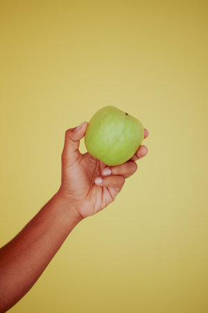 Fresh green apple held up against a yellow backgroundの写真素材