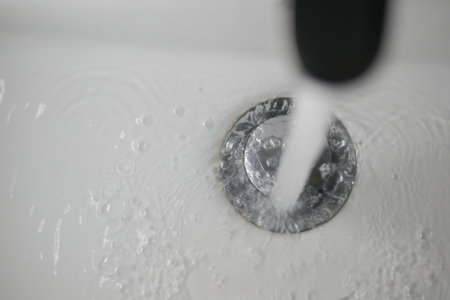 Flowing water from faucet into a white sinkの写真素材