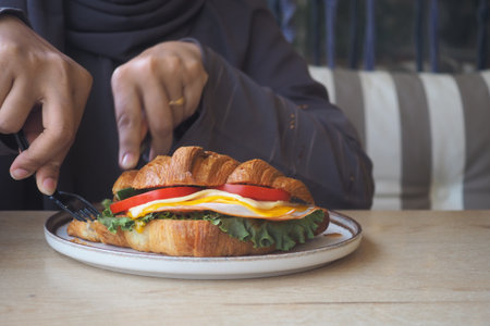 Enjoying a fresh croissant sandwich at a cozy cafeの写真素材