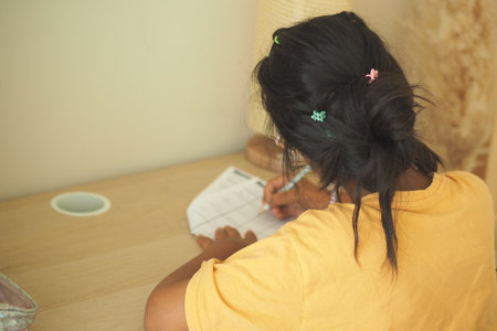 Girl studying with pen at a wooden desk in a cozy spaceの写真素材
