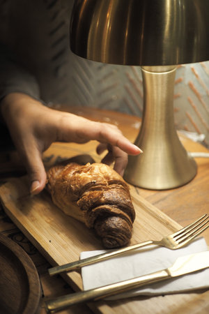 Enjoying a fresh croissant at a cozy cafe tableの写真素材