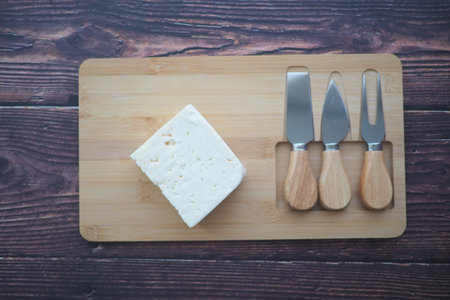 Cheese block and knives on wooden cutting boardの写真素材