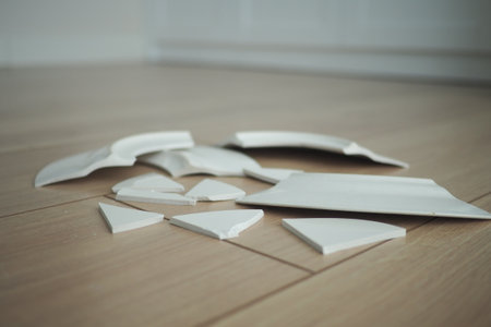 Broken white ceramic pieces scattered on wooden floorの写真素材