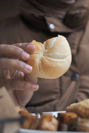 Hand holding a fresh bread roll during a cozy mealの写真素材