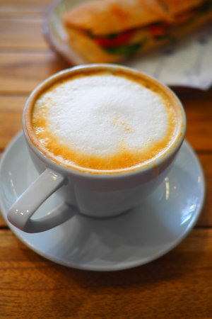 Coffee sits on a table beside a sandwich at a cafeの写真素材