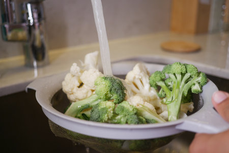 Fresh broccoli and cauliflower being rinsed in kitchenの写真素材