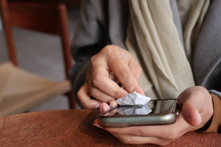 Cleaning a phone screen at a cafe table in the morning light