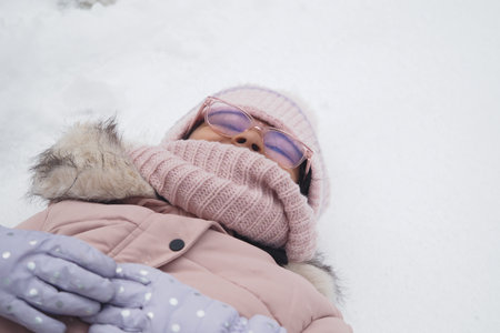 Child enjoying winter by lying in fresh snowの写真素材