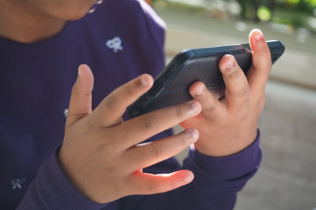 Child focused on smartphone interaction in outdoor settingの写真素材