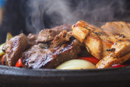 Juicy meats cooking on grill with vegetables in backgroundの写真素材