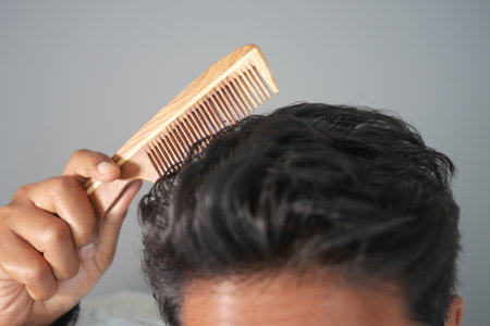 Man combs hair in indoor setting using a wooden combの写真素材