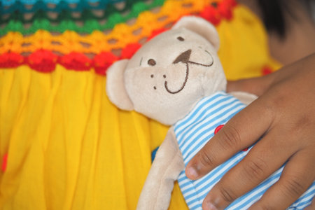 Child holds teddy bear in colorful dressの写真素材