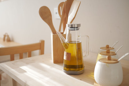 Oil dispenser sits on a table beside wooden spoons and jarsの写真素材