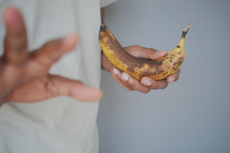 Person holds brown banana and extends hand to the sideの写真素材