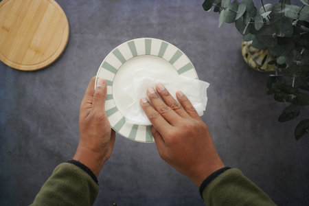Cleaning a plate with a tissue in a kitchen settingの写真素材