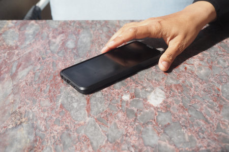 Hand reaching for a smartphone on a table surface