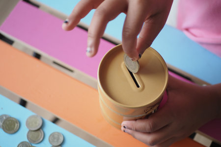 Child inserts coin into savings box on colorful table