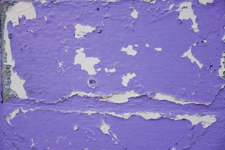 Old wall with purple paint and peeling surface in sunlightの写真素材