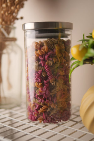 Colorful pasta in a glass jar on a kitchen shelf
