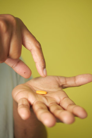 Person holds yellow pill in hand, green background