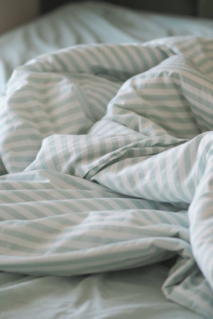 The bed has wrinkled blankets and sheets in light colors