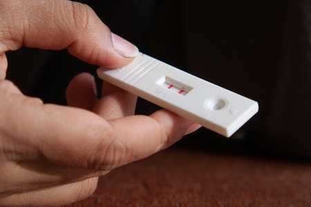 A hand holds a pregnancy test kit showing two visible lines