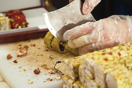 A person cuts turkish delight with a knife while wearing gloves in a shopの写真素材